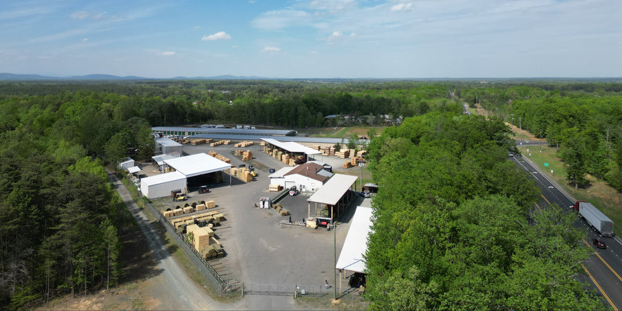 Aerial view of a large outdoor storage facility with trucks and equipment, surrounded by trees under a blue sky.
